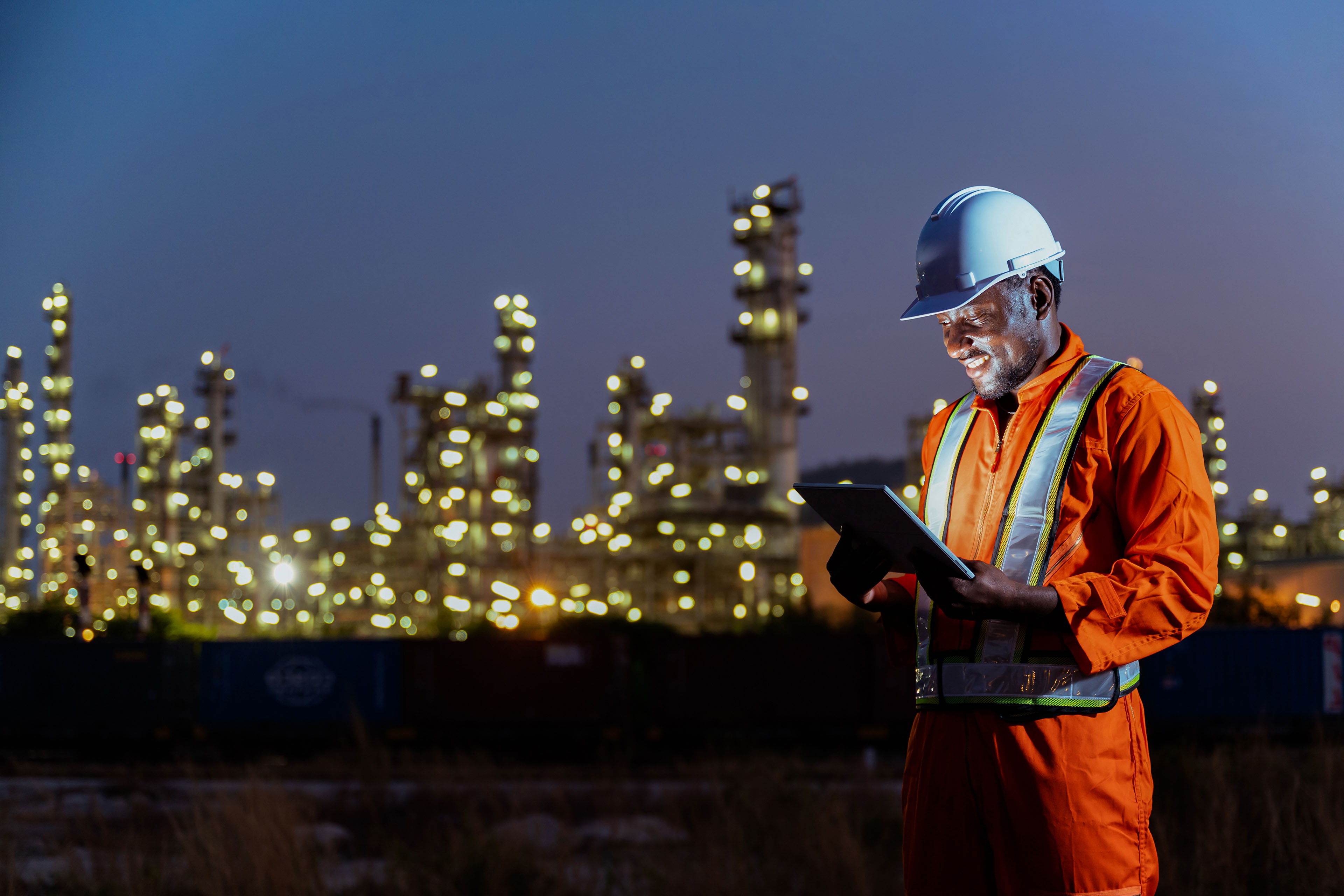 African construction engineer working on tablet inspecting the build project in oil refinery plant at night