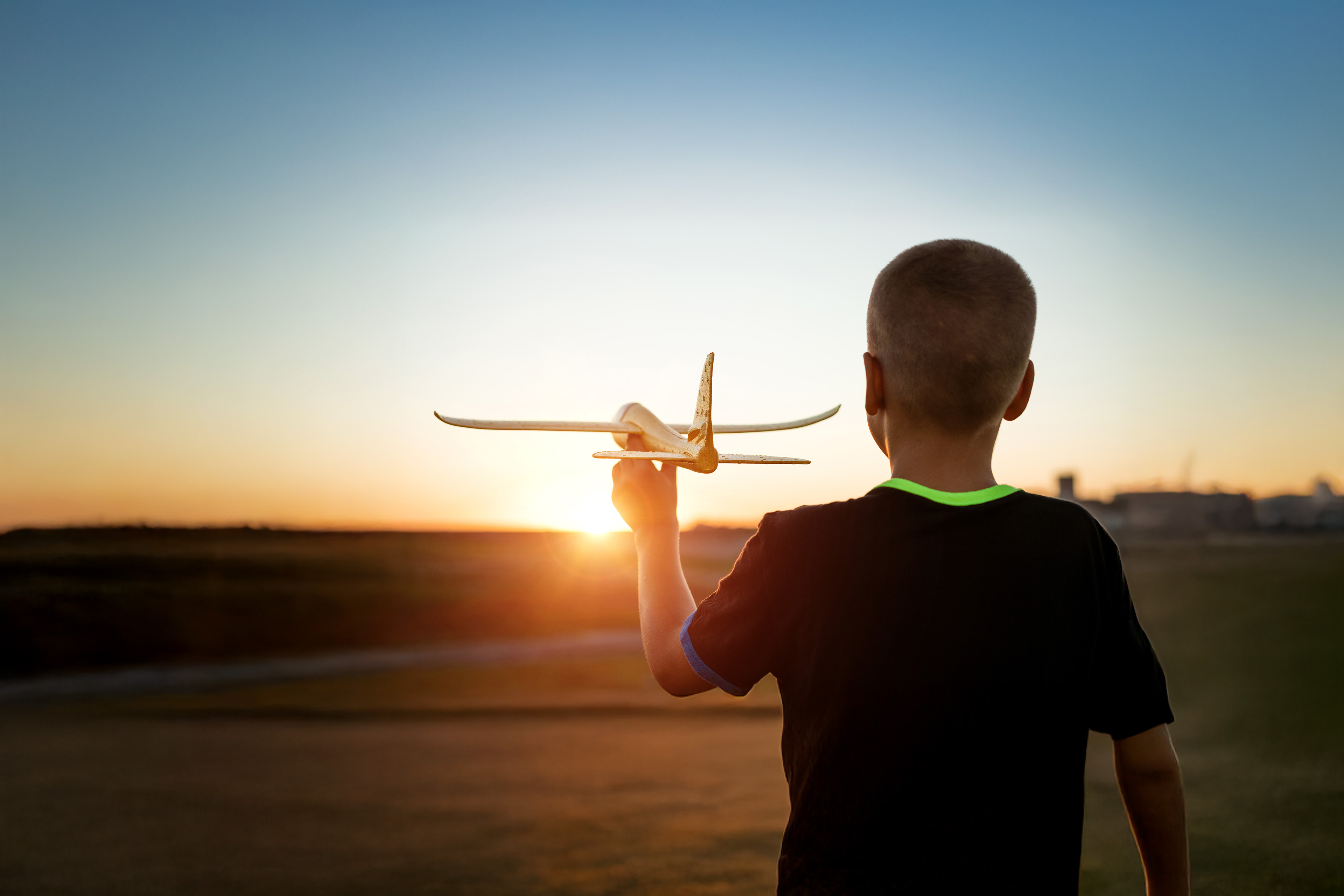 Boy throws a toy airplane in the summer at sunset